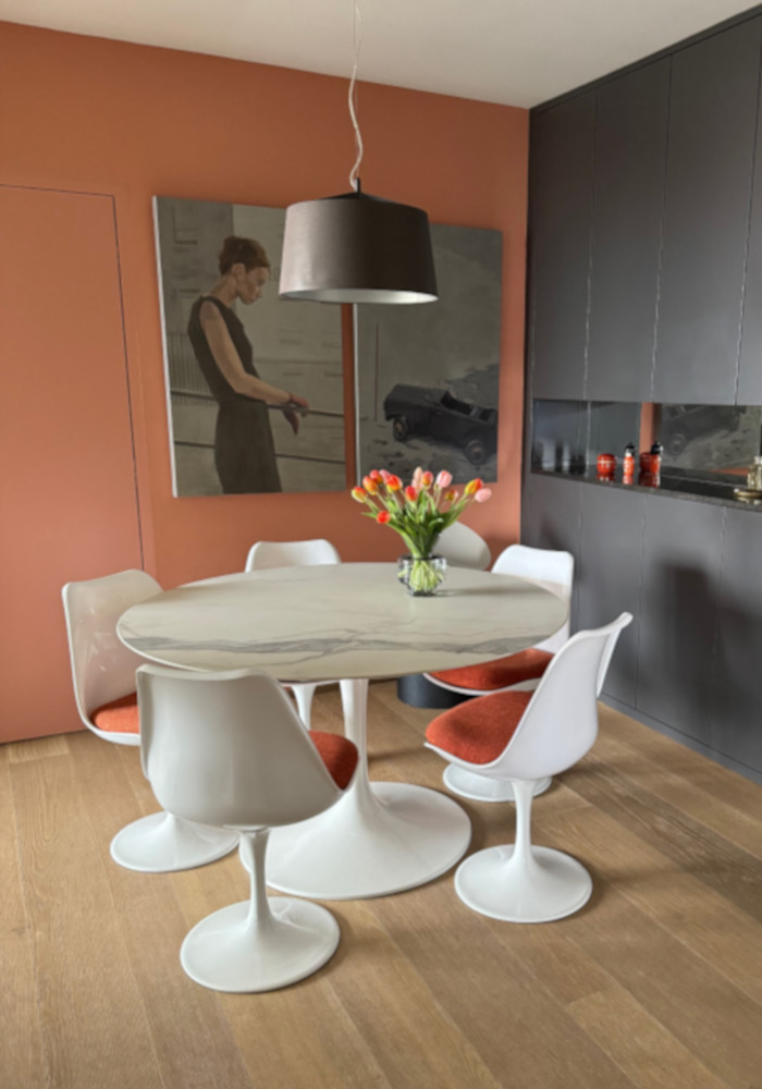 Salle à manger contemporaine avec table ronde en marbre, chaises Tulip blanches et bouquet de tulipes, dans un intérieur au design épuré.